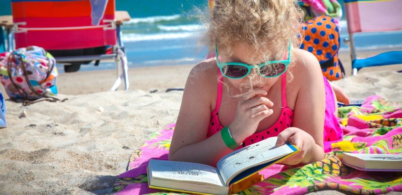 Una joven leyendo un libro en la playa